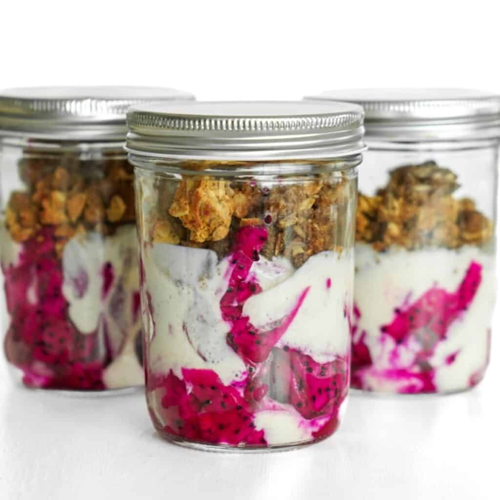 Three beautifully layered breakfast granola cups filled with fresh dragonfruit, probiotic tofu yogurt, and homemade protein granola.