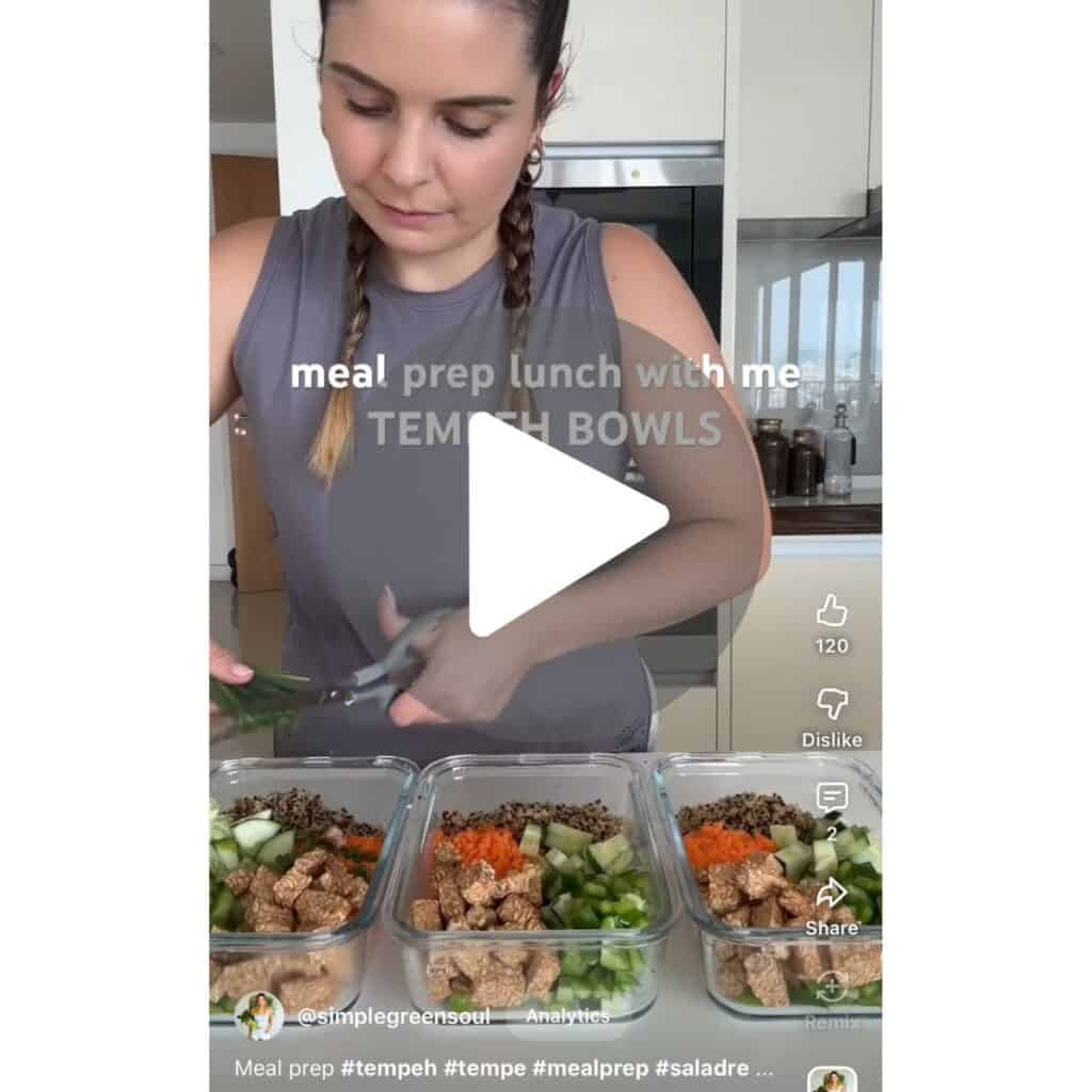 Vertical video screenshot of a YouTube Short titled "TEMPEH BOWLS", showing glass meal prep containers filled with cooked quinoa, grated carrots, diced cucumbers, and crispy tempeh blocks lined up on a kitchen counter.