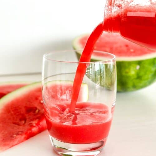 Fresh electrolyte restoring watermelon juice pouring from a glass pitcher into a drinking glass with fresh watermelon slices in the background.