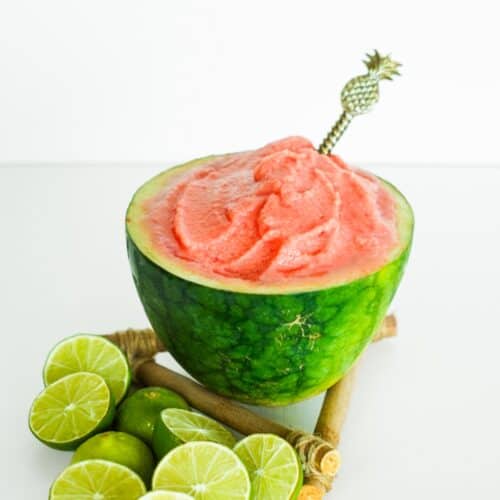 Scooped creamy watermelon sorbet served inside a fresh watermelon shell, garnished with lime halves.