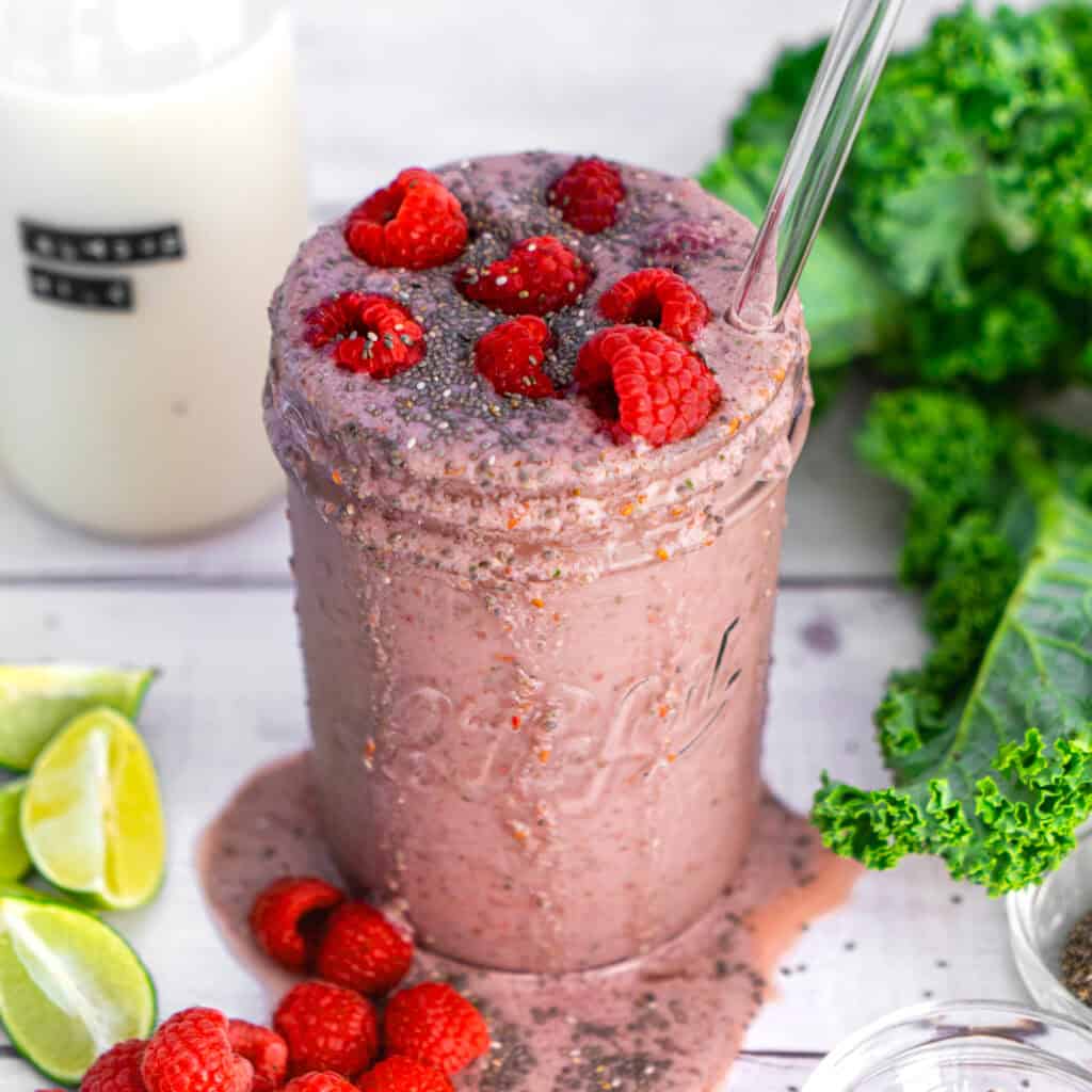 A bright pink raspberry banana smoothie in a glass jar topped with fresh raspberries and a squeeze of lime.