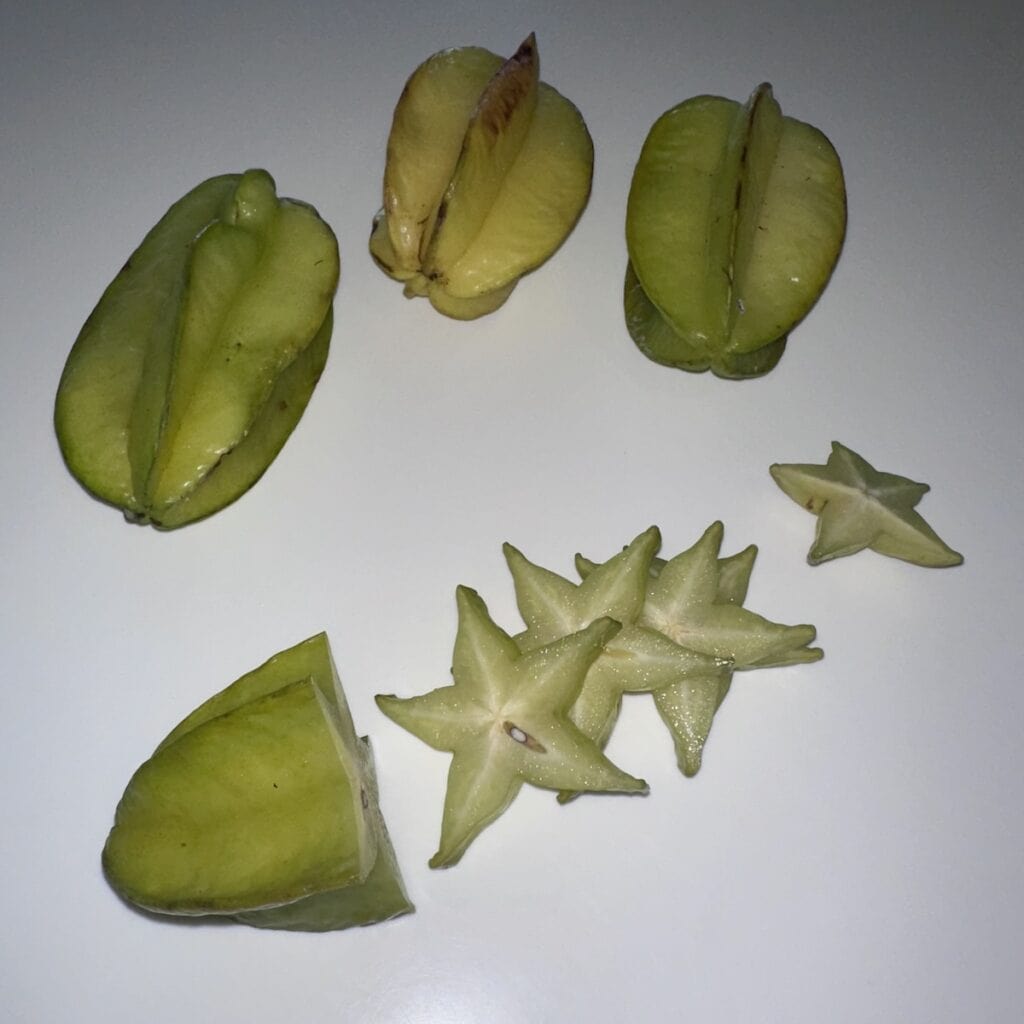 a bunch of green starfruit, as well as sliced green startfruit, exposing the crunchy interior and star shape