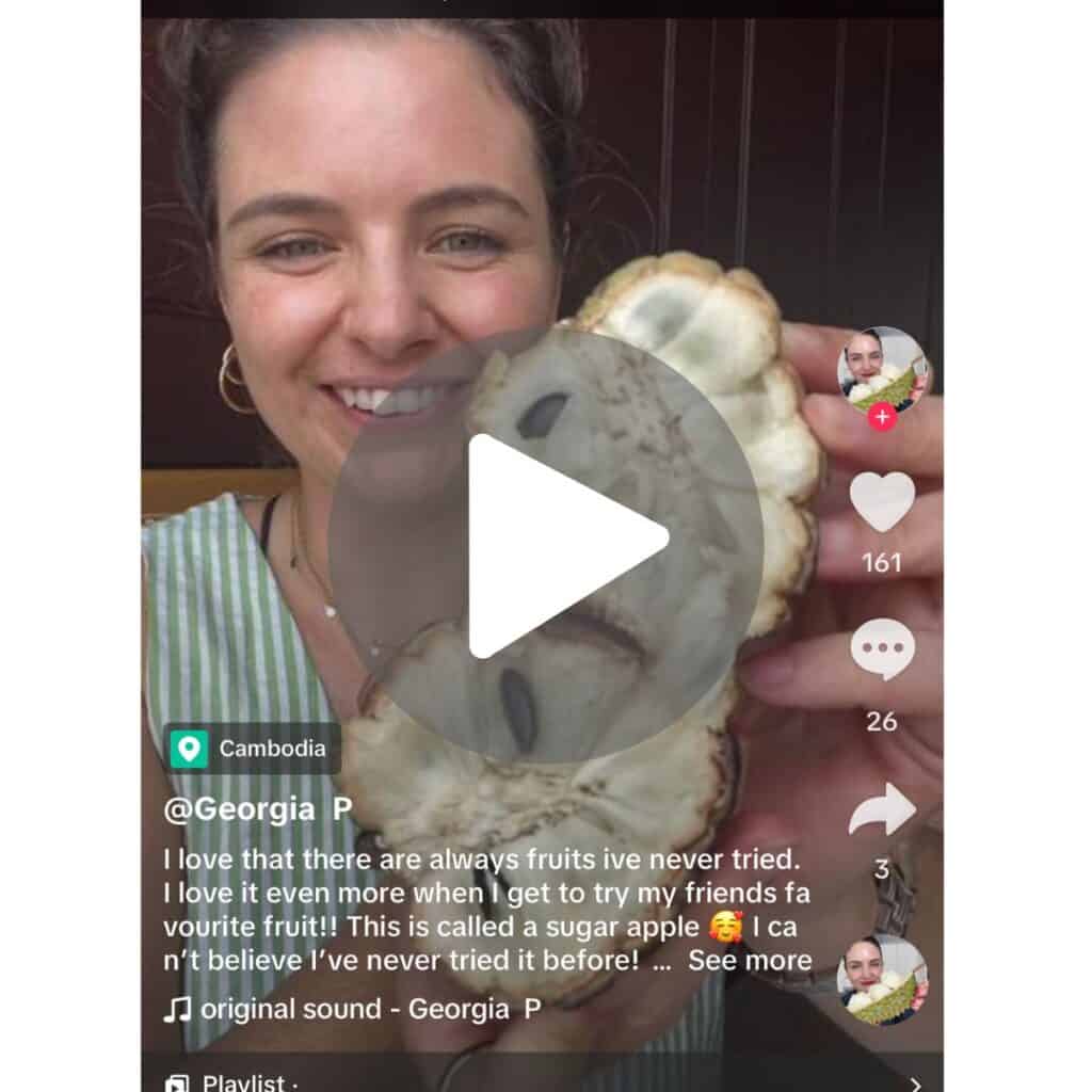 a screenshot of a tiktok video of a girl holding a soursop, sliced in hald, exposing the creamy interior and black seeds