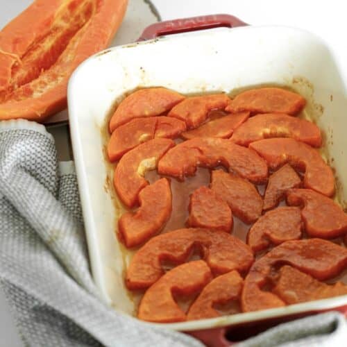 ripe sliced baked papaya in a baking tray with butter and coconut sugar