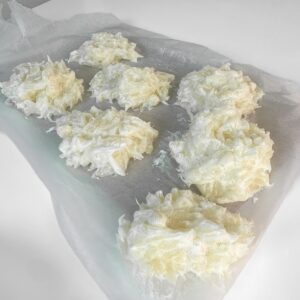 A close-up shot of individual spoonfuls of the pomelo yogurt mixture spaced out on a baking tray lined with parchment paper, ready to be frozen into yogurt bites.