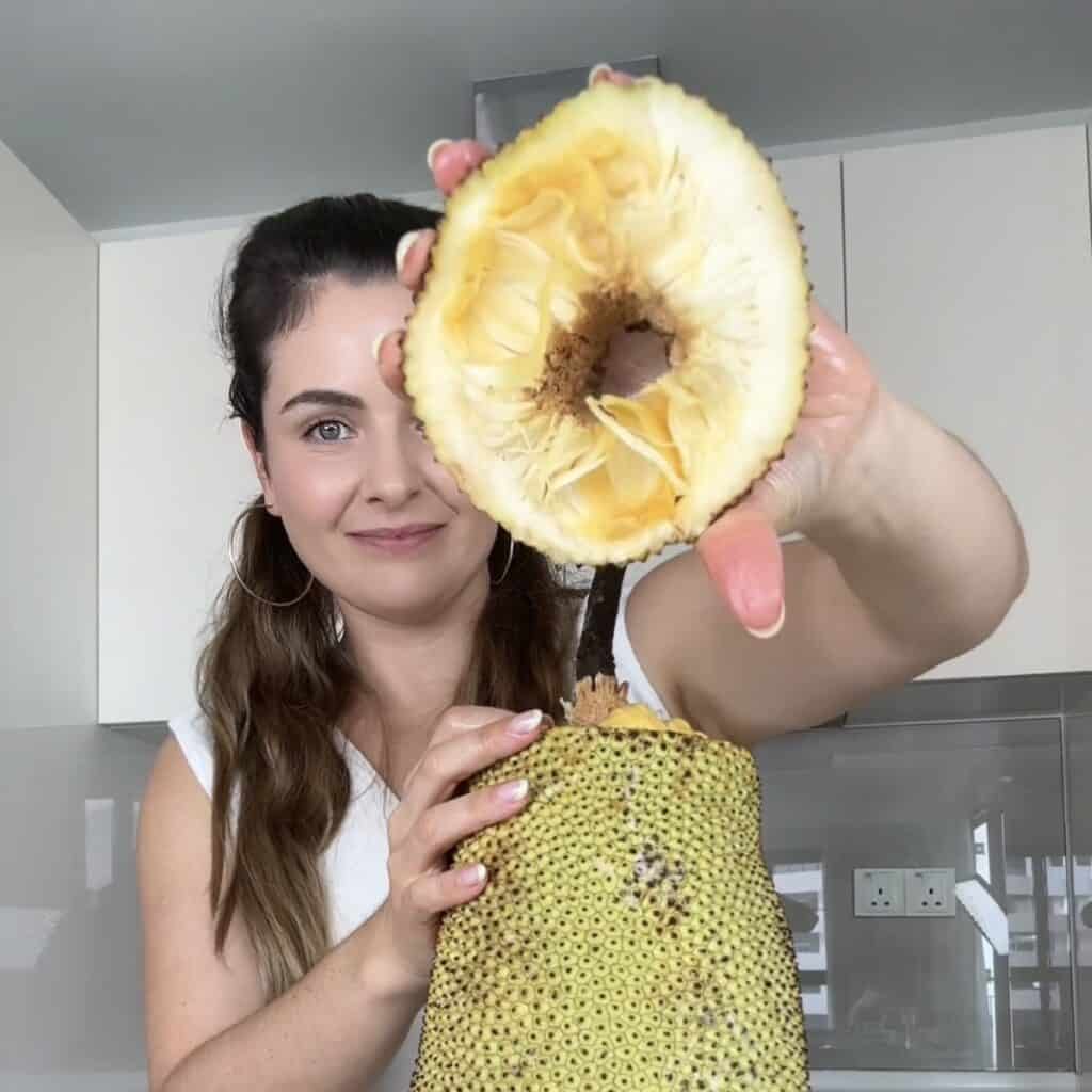 A close-up of a person holding the sliced top rind section or "hat" of a cempedak fruit in the kitchen, demonstrating the first step of opening it.