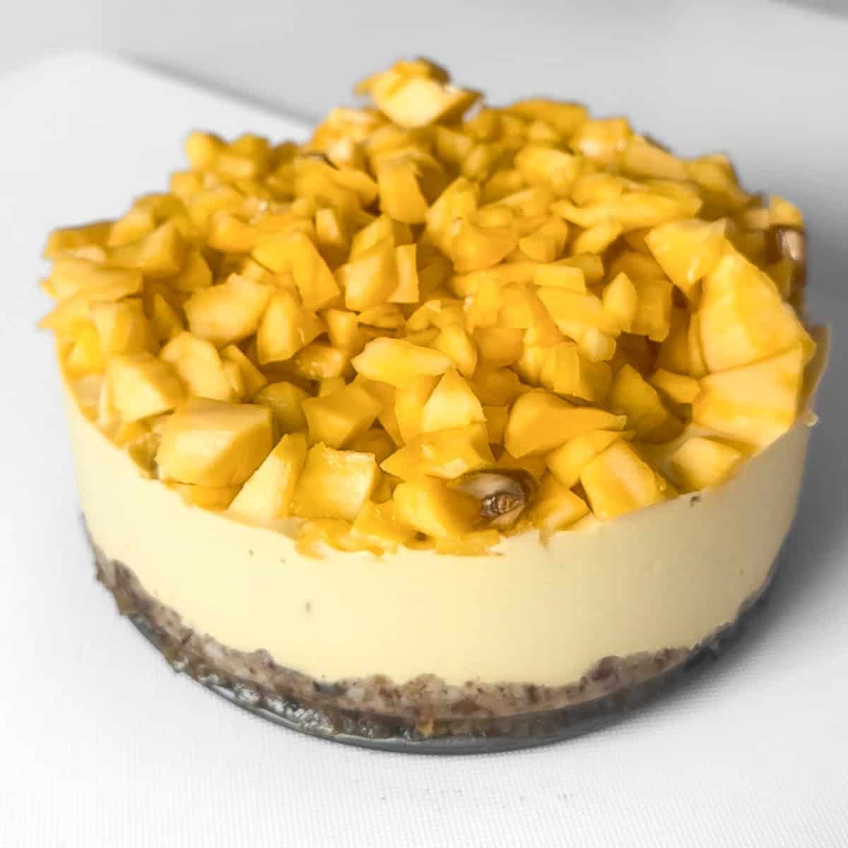 A whole, unsliced no-bake dairy-free jackfruit cheesecake, presenting its circular creaminess piled high with fresh, vibrant, diced tropical honey jackfruit flesh.
