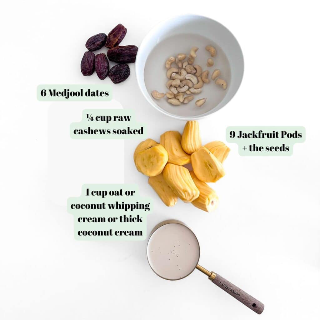 A flat-lay layout of the ingredients for a dairy-free jackfruit cheesecake, including fresh yellow jackfruit pods, pitted Medjool dates, a bowl of raw cashews, and coconut whipping cream next to a measuring cup.