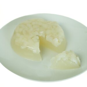 A close-up of a clear, homemade Coconut Rambutan Jelly pudding on a plate, sliced open to reveal the juicy, white rambutan fruit pieces suspended inside.