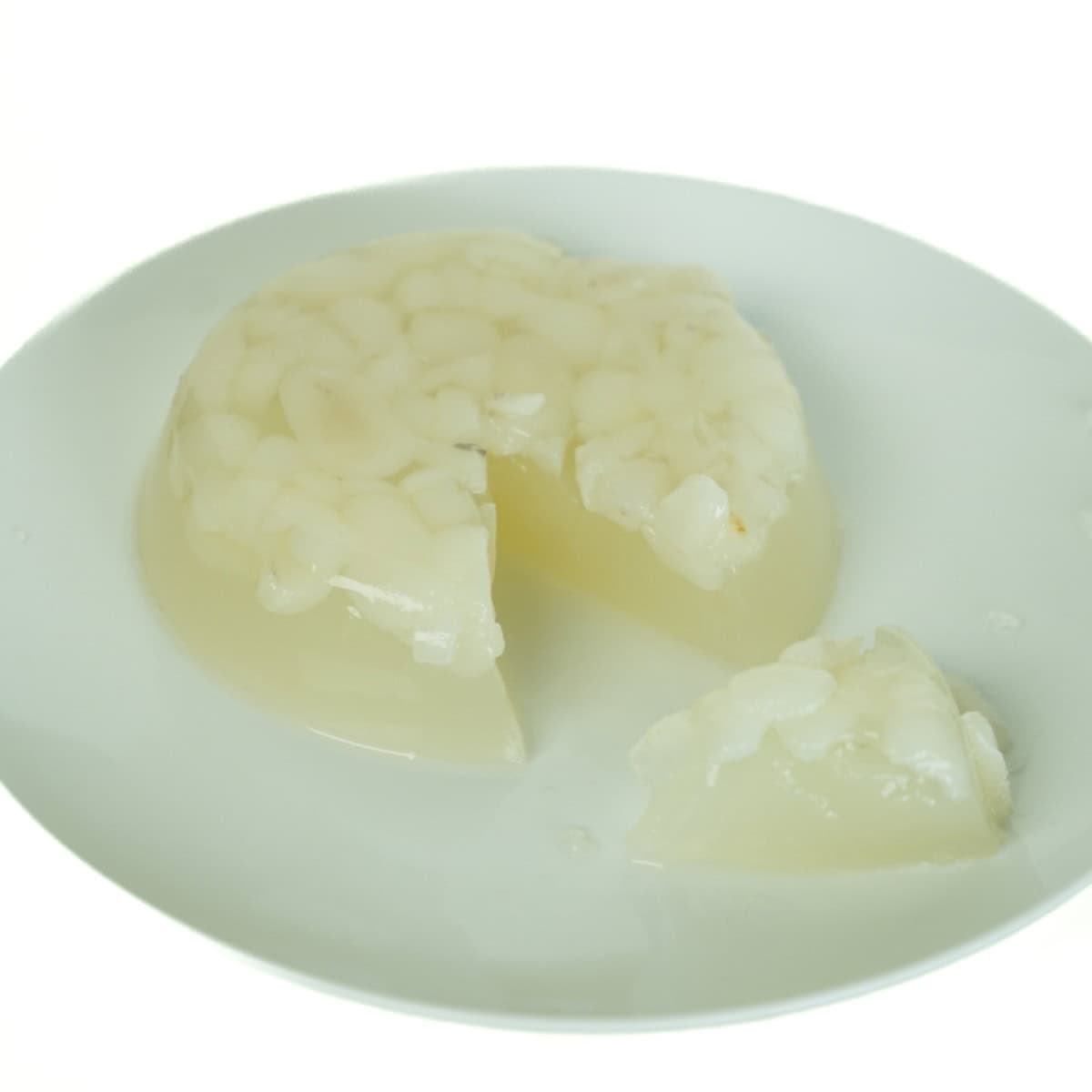 A close-up of a clear, homemade Coconut Rambutan Jelly pudding on a plate, sliced open to reveal the juicy, white rambutan fruit pieces suspended inside.