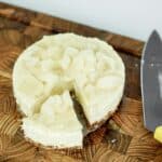 A top-down view of a sliced, no-bake vegan rambutan cheesecake on a wooden cutting board, showcasing its creamy tropical filling and crumbly date-cashew crust.