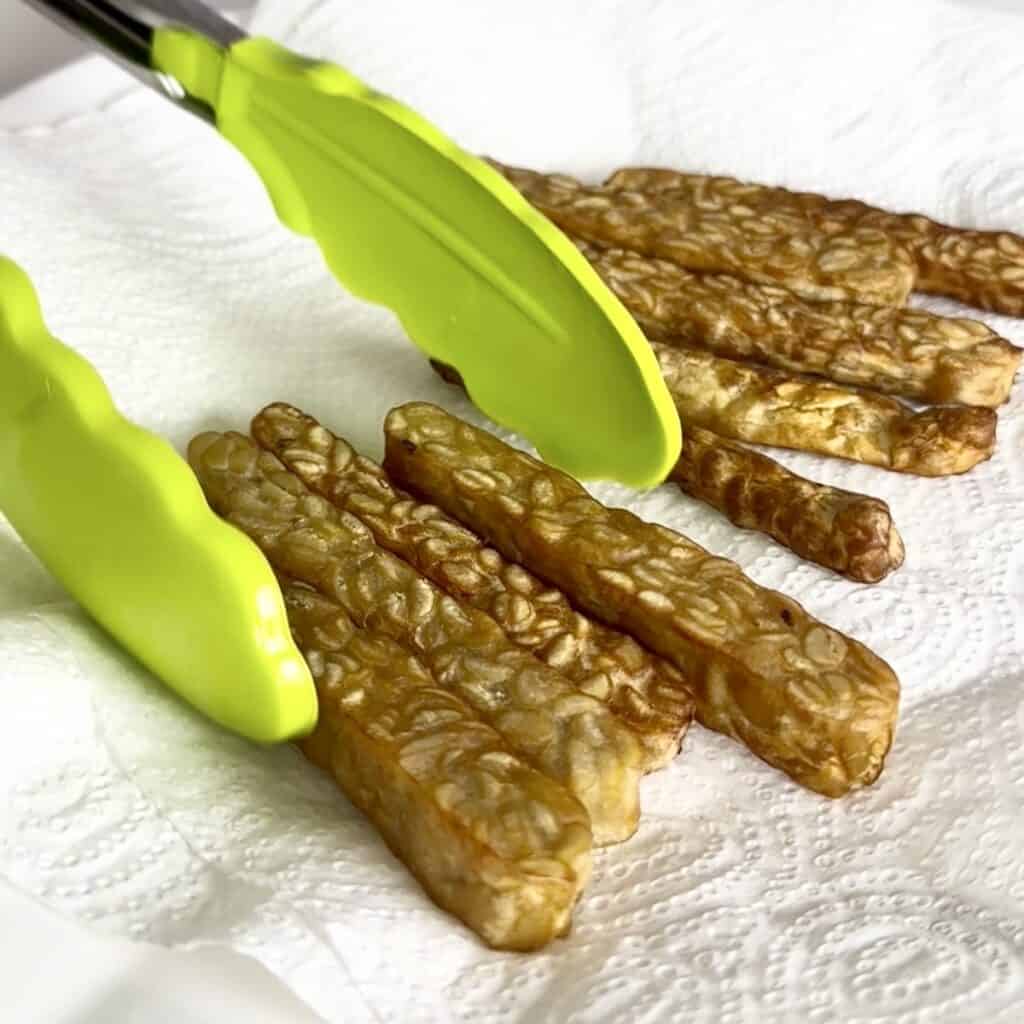 Golden, crispy shallow fried tempeh slices in a hot skillet.