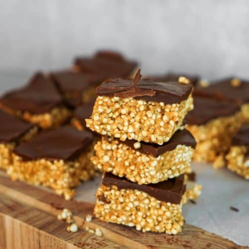 Healthy rice crispy treats with peanut butter made from quinoa puffs, maple syrup, hemp hearts and dark chocolate stacked on a wooden board.