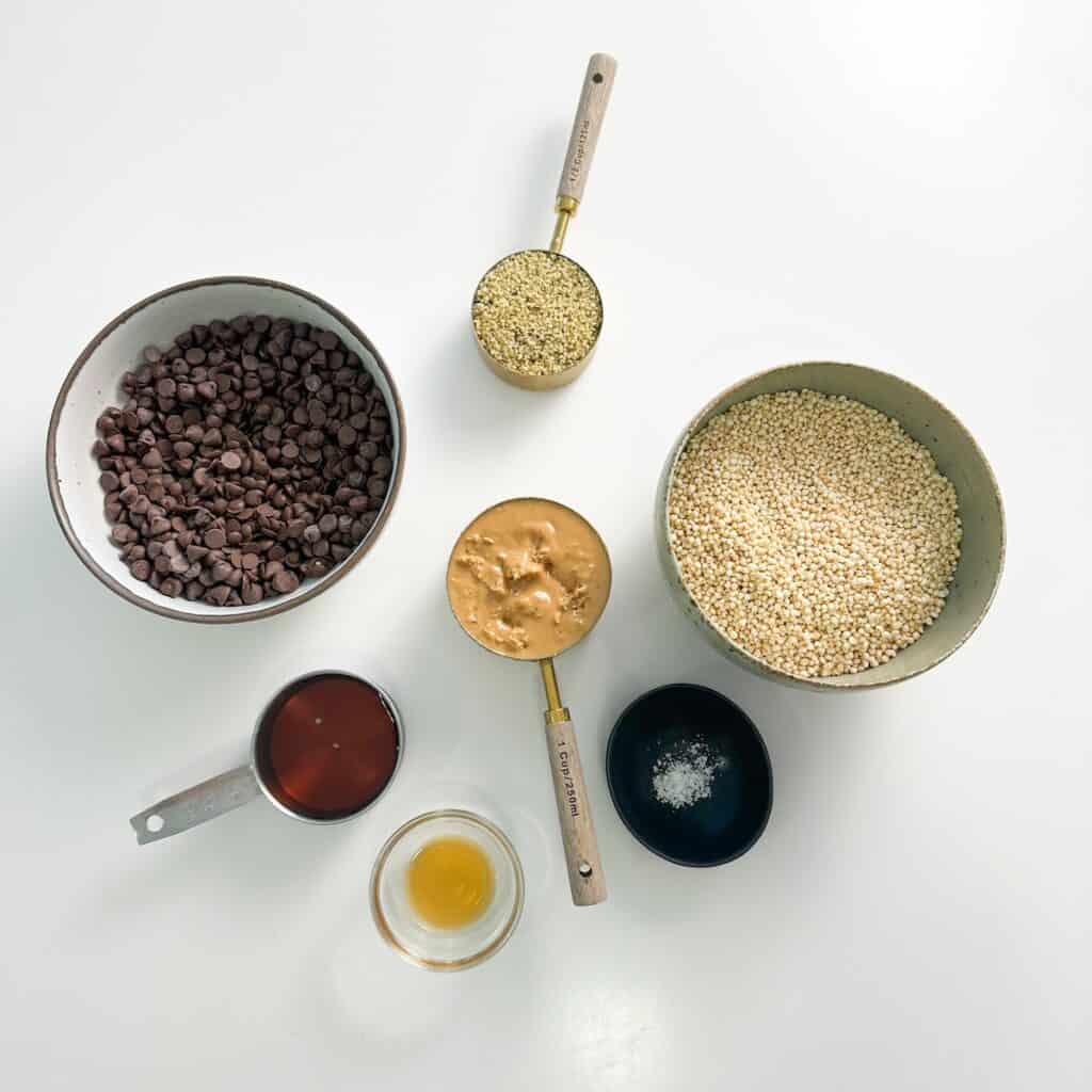 Ingredients for a healthy rice crispy treats recipe including quinoa puffs, peanut butter, hemp hearts, maple syrup, vanilla, dark chocolate chips and salt.