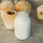 Creamy coconut shake made with fresh coconut water and coconut meat served in a mason jar with young coconuts in the background.